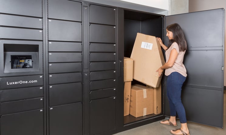 A woman removes a large package from the floor-to-ceiling Luxer One oversized locker. Four other packages remain inside the locker.