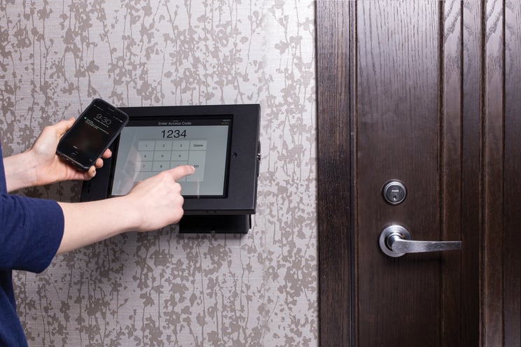 Resident holding a smartphone enters their code on the iPad touchscreen mounted on the wall.