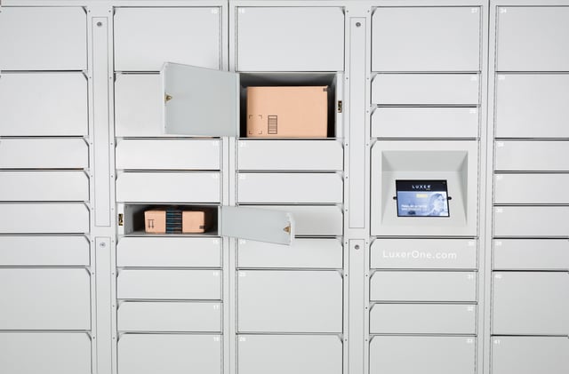 Front view of white Luxer One package lockers. A small and medium locker are open, revealing cardboard package boxes.