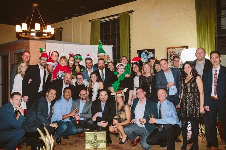 A group of smiling people pose with holiday hats and costume pieces for the Luxer One holiday photo. 